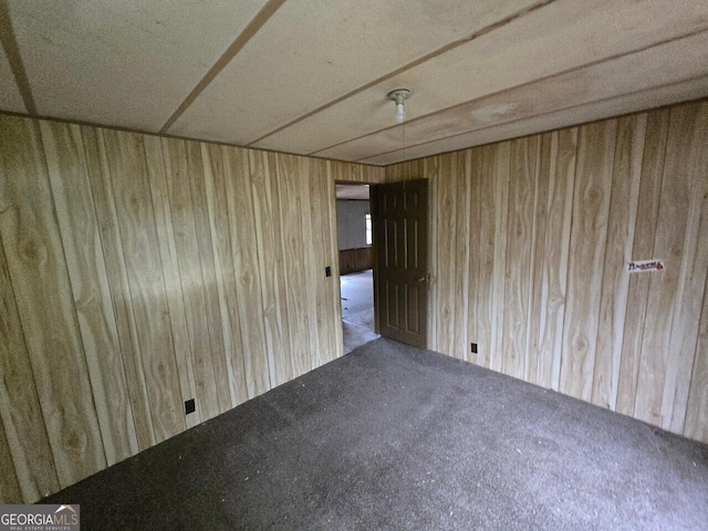 carpeted empty room featuring wooden walls