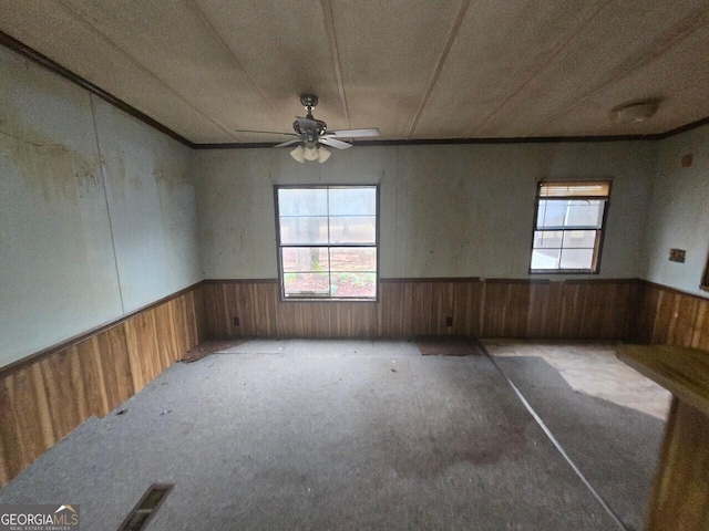 unfurnished room featuring carpet floors, wainscoting, ceiling fan, and wooden walls