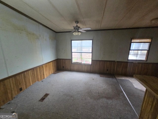 carpeted spare room featuring a ceiling fan, wainscoting, wood walls, and visible vents