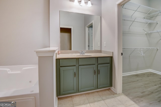 full bath featuring a walk in closet, a jetted tub, tile patterned flooring, baseboards, and vanity