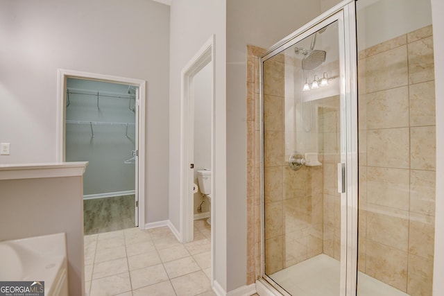 bathroom featuring tile patterned floors, a spacious closet, a stall shower, and toilet