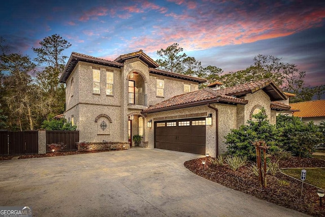 mediterranean / spanish home with an attached garage, a balcony, a tile roof, fence, and concrete driveway