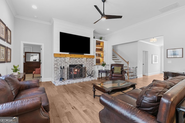 living area with stairway, wood finished floors, a ceiling fan, visible vents, and a brick fireplace