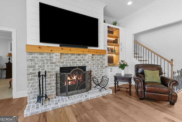 living area featuring stairway, wood finished floors, baseboards, a fireplace, and ornamental molding