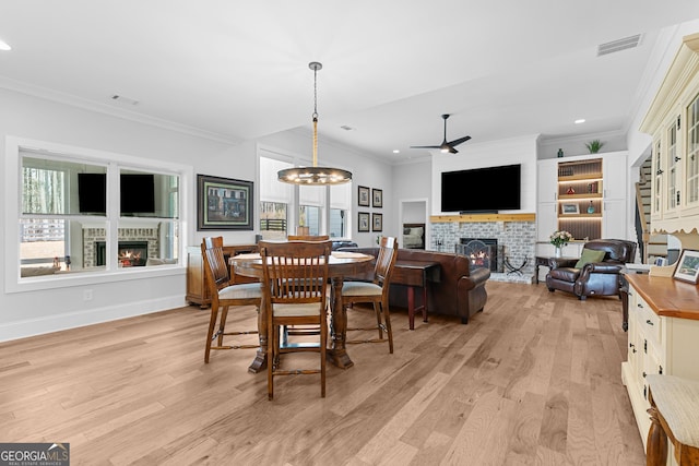 dining room with visible vents, a brick fireplace, light wood-style flooring, and ceiling fan with notable chandelier