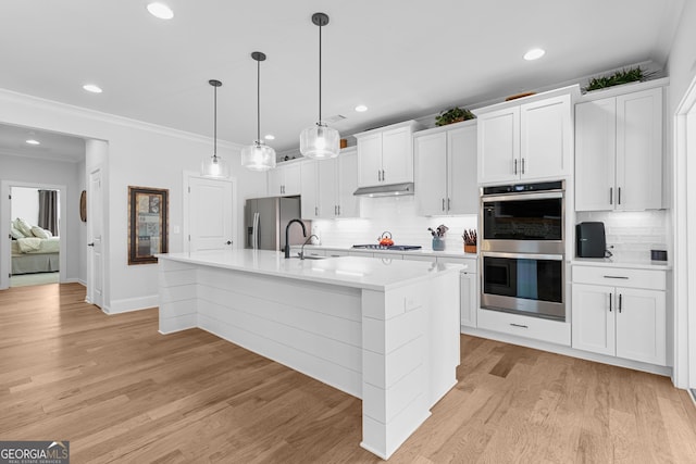 kitchen with a sink, light countertops, under cabinet range hood, appliances with stainless steel finishes, and light wood-type flooring