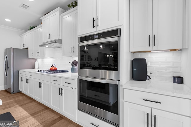 kitchen featuring tasteful backsplash, under cabinet range hood, light wood-style flooring, appliances with stainless steel finishes, and white cabinetry