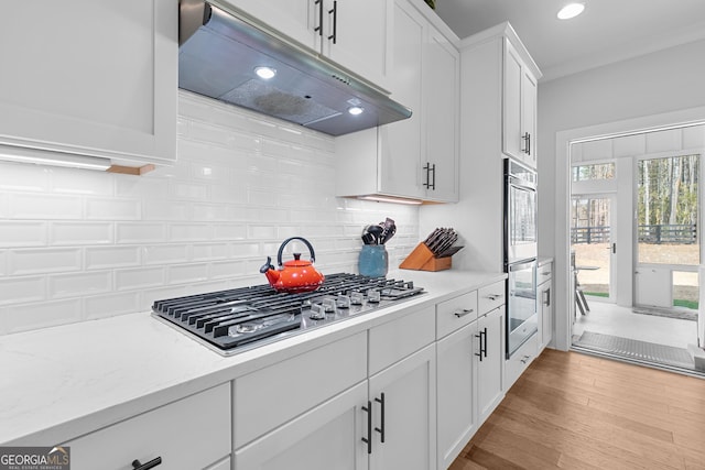 kitchen with under cabinet range hood, wood finished floors, stainless steel appliances, white cabinets, and decorative backsplash