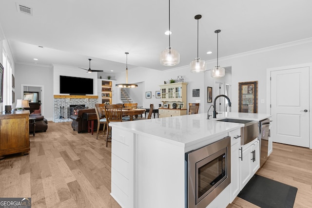 kitchen featuring ornamental molding, a sink, a warm lit fireplace, stainless steel appliances, and ceiling fan