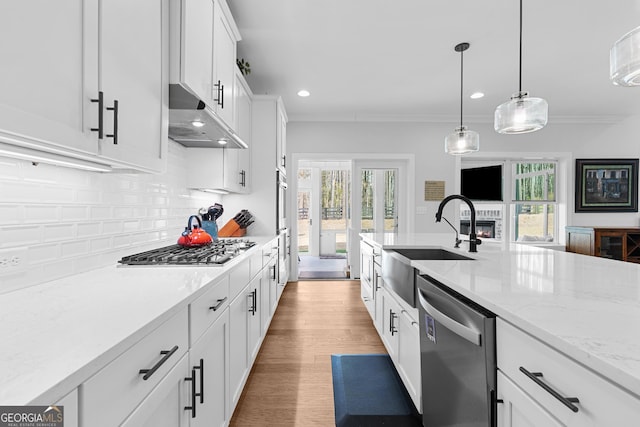 kitchen with tasteful backsplash, under cabinet range hood, appliances with stainless steel finishes, white cabinetry, and a sink