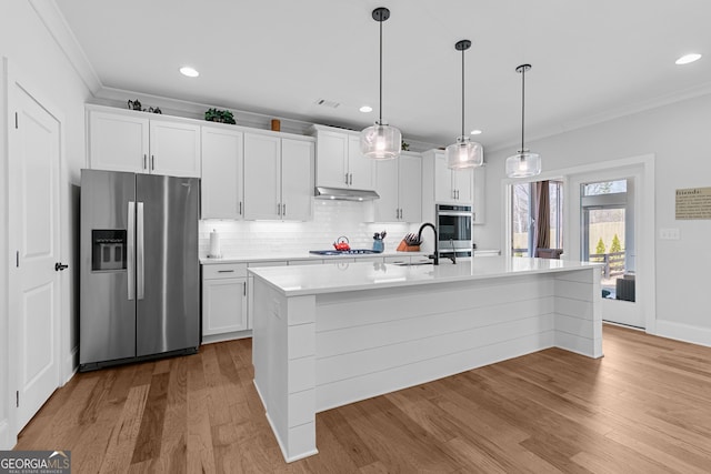 kitchen with under cabinet range hood, a sink, appliances with stainless steel finishes, crown molding, and light countertops