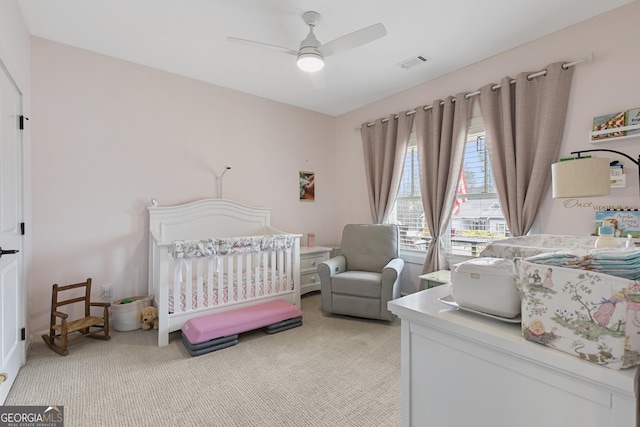 bedroom with a nursery area, visible vents, light colored carpet, and ceiling fan