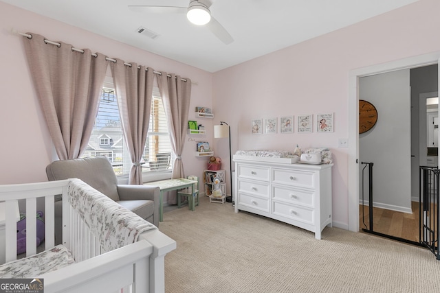 bedroom with baseboards, visible vents, ceiling fan, a nursery area, and light colored carpet