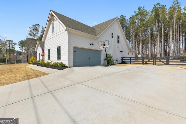 view of side of home featuring board and batten siding, a shingled roof, fence, driveway, and a gate