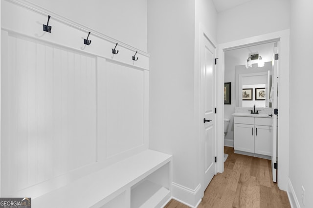 mudroom featuring baseboards, light wood finished floors, and a sink