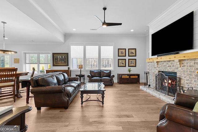 living area with light wood finished floors, a fireplace, ceiling fan, and ornamental molding