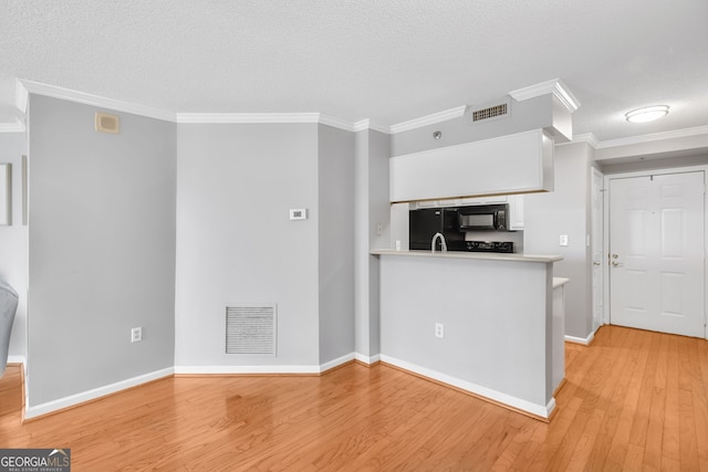 kitchen featuring light wood-type flooring, black appliances, visible vents, and crown molding