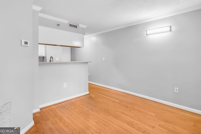 unfurnished room featuring baseboards, visible vents, light wood-style flooring, ornamental molding, and a textured ceiling