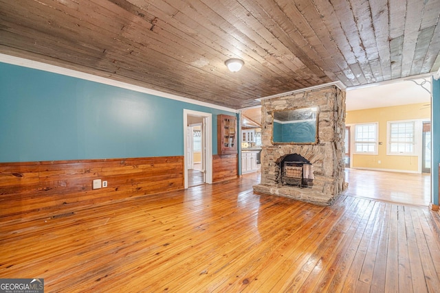 unfurnished living room with wooden ceiling, a fireplace, wainscoting, wood-type flooring, and crown molding