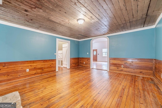 spare room with arched walkways, wooden walls, a wainscoted wall, wood ceiling, and ornamental molding