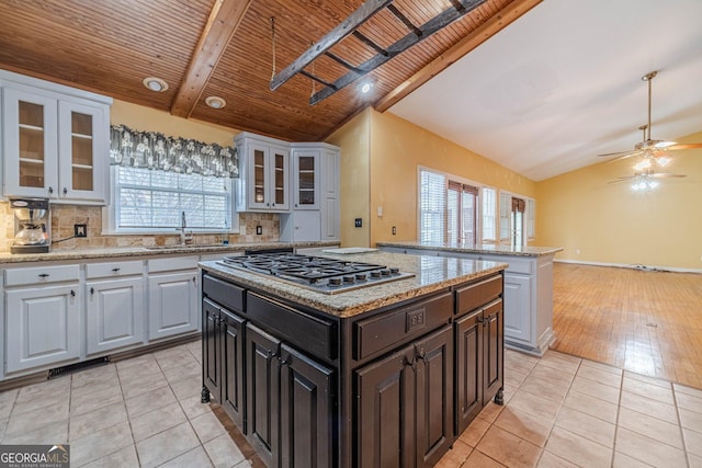 kitchen featuring light tile patterned floors, lofted ceiling with beams, a center island, stainless steel gas stovetop, and backsplash