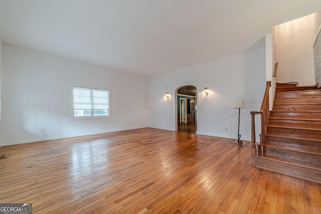 unfurnished living room with arched walkways, stairway, light wood-style flooring, and baseboards