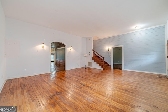 unfurnished living room with arched walkways, visible vents, baseboards, stairs, and light wood-style floors