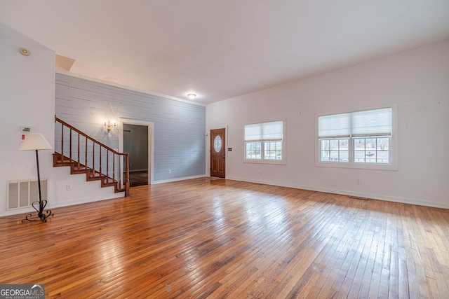 unfurnished living room with hardwood / wood-style flooring, visible vents, baseboards, and stairs