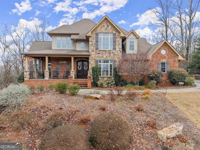 craftsman-style home with stone siding, roof with shingles, a porch, and brick siding