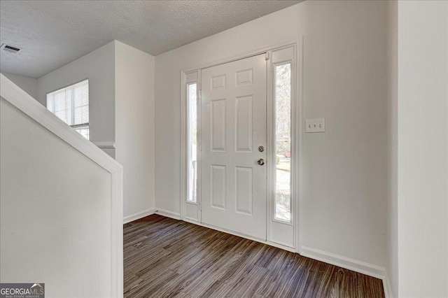 foyer entrance featuring a healthy amount of sunlight, a textured ceiling, visible vents, and wood finished floors