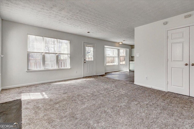 carpeted empty room featuring a textured ceiling, washer / clothes dryer, and baseboards