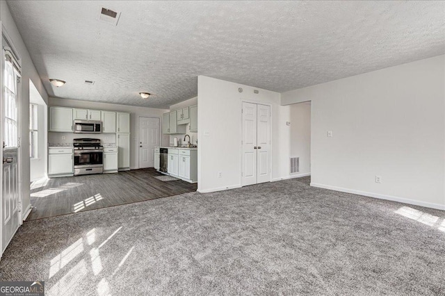 unfurnished living room featuring a textured ceiling, dark carpet, visible vents, and baseboards