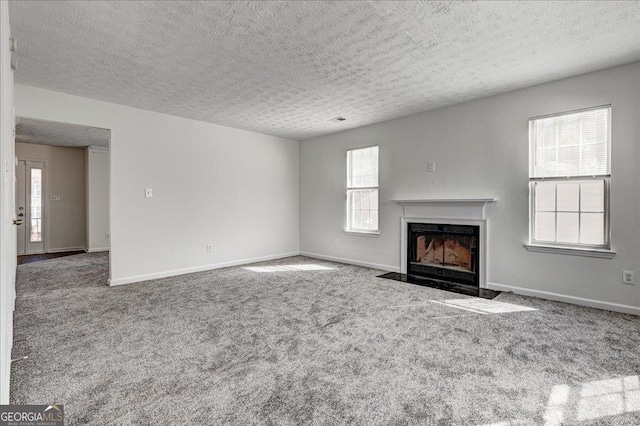 unfurnished living room with carpet floors, a fireplace with flush hearth, baseboards, and a textured ceiling