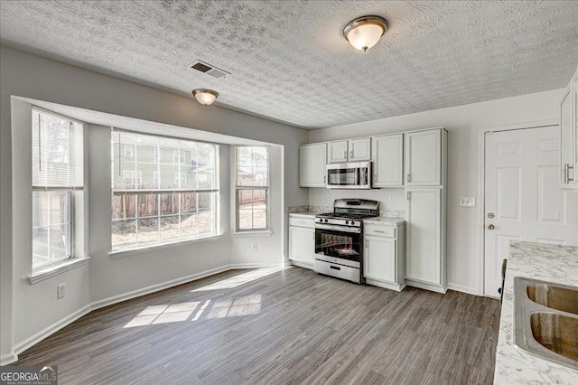 kitchen featuring stainless steel appliances, visible vents, a sink, wood finished floors, and baseboards