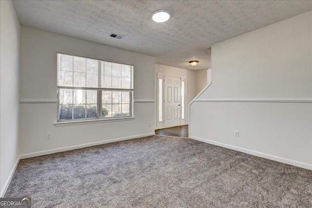 carpeted empty room featuring a textured ceiling, visible vents, and baseboards