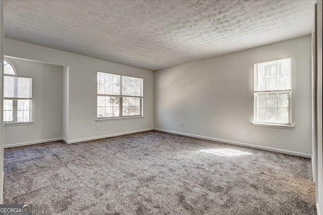 empty room with carpet, baseboards, and a textured ceiling