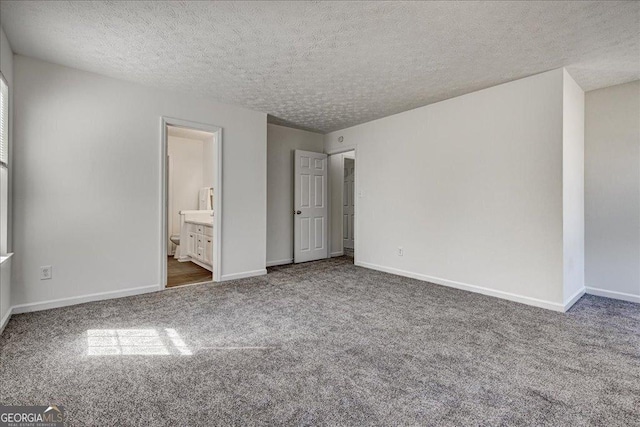 unfurnished bedroom featuring ensuite bath, a textured ceiling, baseboards, and carpet flooring