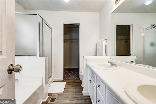 full bathroom featuring a stall shower, a sink, a textured ceiling, wood finished floors, and a bath