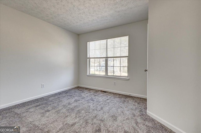 empty room featuring visible vents, carpet flooring, a textured ceiling, and baseboards