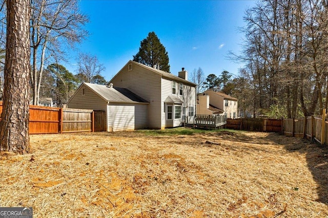 back of house with a deck, a fenced backyard, and a chimney