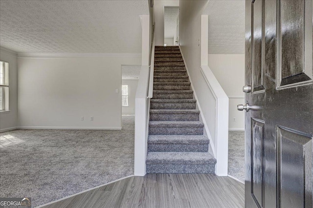 stairway featuring carpet, ornamental molding, a textured ceiling, and wood finished floors