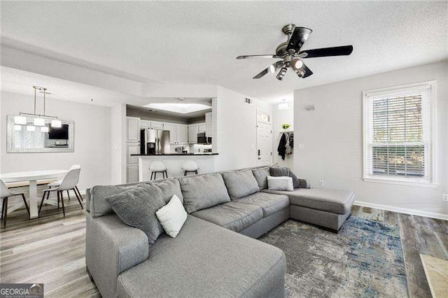 living area with a textured ceiling, light wood-type flooring, a ceiling fan, and baseboards