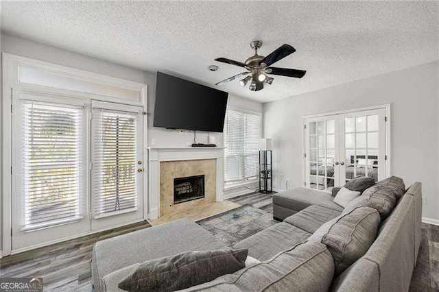 living area featuring a ceiling fan, a tile fireplace, wood finished floors, a textured ceiling, and french doors