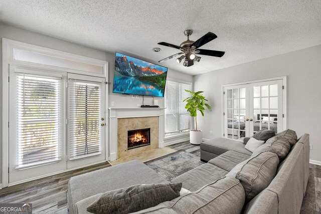 living room featuring wood finished floors, ceiling fan, a tile fireplace, french doors, and a textured ceiling