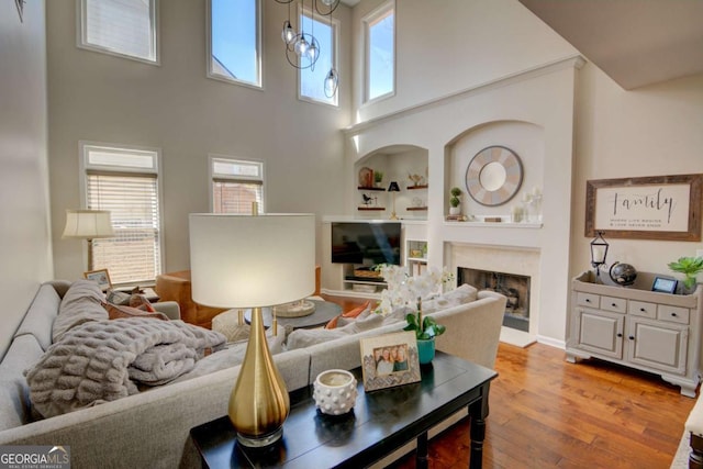 living room with built in features, light wood-style flooring, a high ceiling, a fireplace, and a chandelier