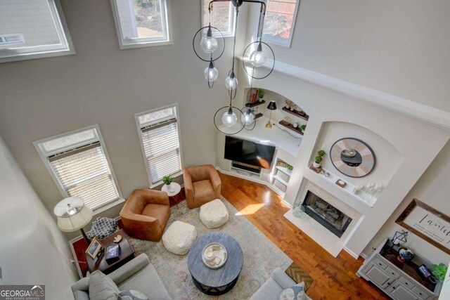 living area featuring a towering ceiling, plenty of natural light, a fireplace with flush hearth, and wood finished floors