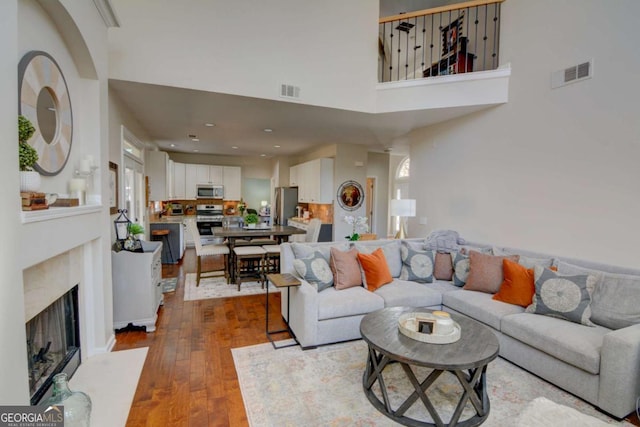 living room with a towering ceiling, a fireplace with flush hearth, visible vents, and dark wood-style flooring