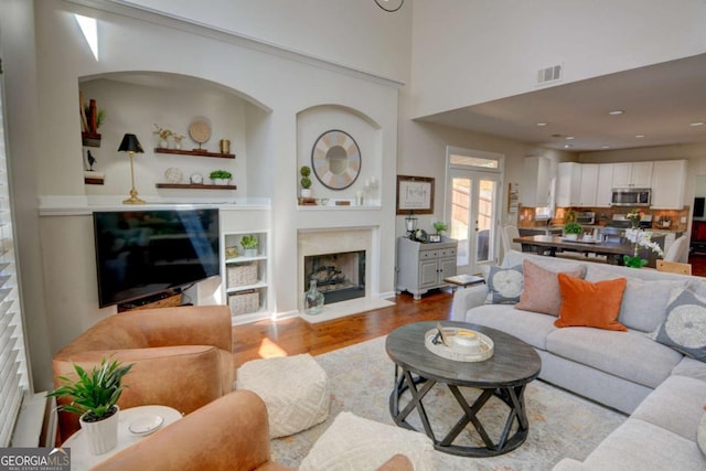 living room featuring visible vents, a fireplace with raised hearth, and wood finished floors