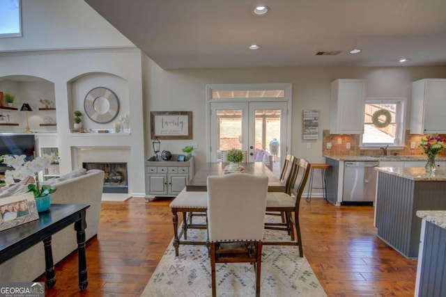 dining area featuring a fireplace with raised hearth, french doors, wood-type flooring, and recessed lighting