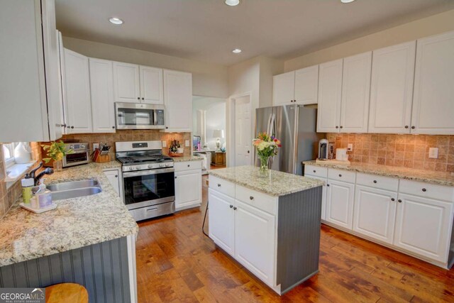 kitchen featuring wood finished floors, appliances with stainless steel finishes, a kitchen island, and a sink